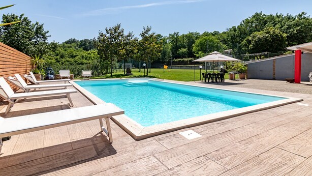 A rectangular swimming pool with a wooden deck, surrounded by lounge chairs and a table with umbrellas. - Vacation Villa "La Quercia★ Swimming Pool-BBQ-Nature (Carbognano)