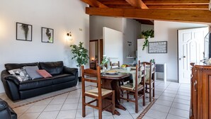 A living room with a black leather sofa, wooden dining table, and chairs. There are framed pictures on the wall, a potted plant, and a white door. - Vacation Villa "La Quercia★ Swimming Pool-BBQ-Nature (Carbognano)