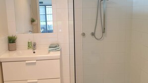 A modern bathroom with a glass shower enclosure, a white vanity with a mirror, and a potted plant. - 5 min walk to the Beach! (Rosebud)