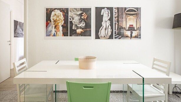 A dining area with a white table, green chairs, and three framed artworks on the wall.