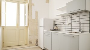 A kitchen with white cabinets, a stainless steel kettle, and a sink.