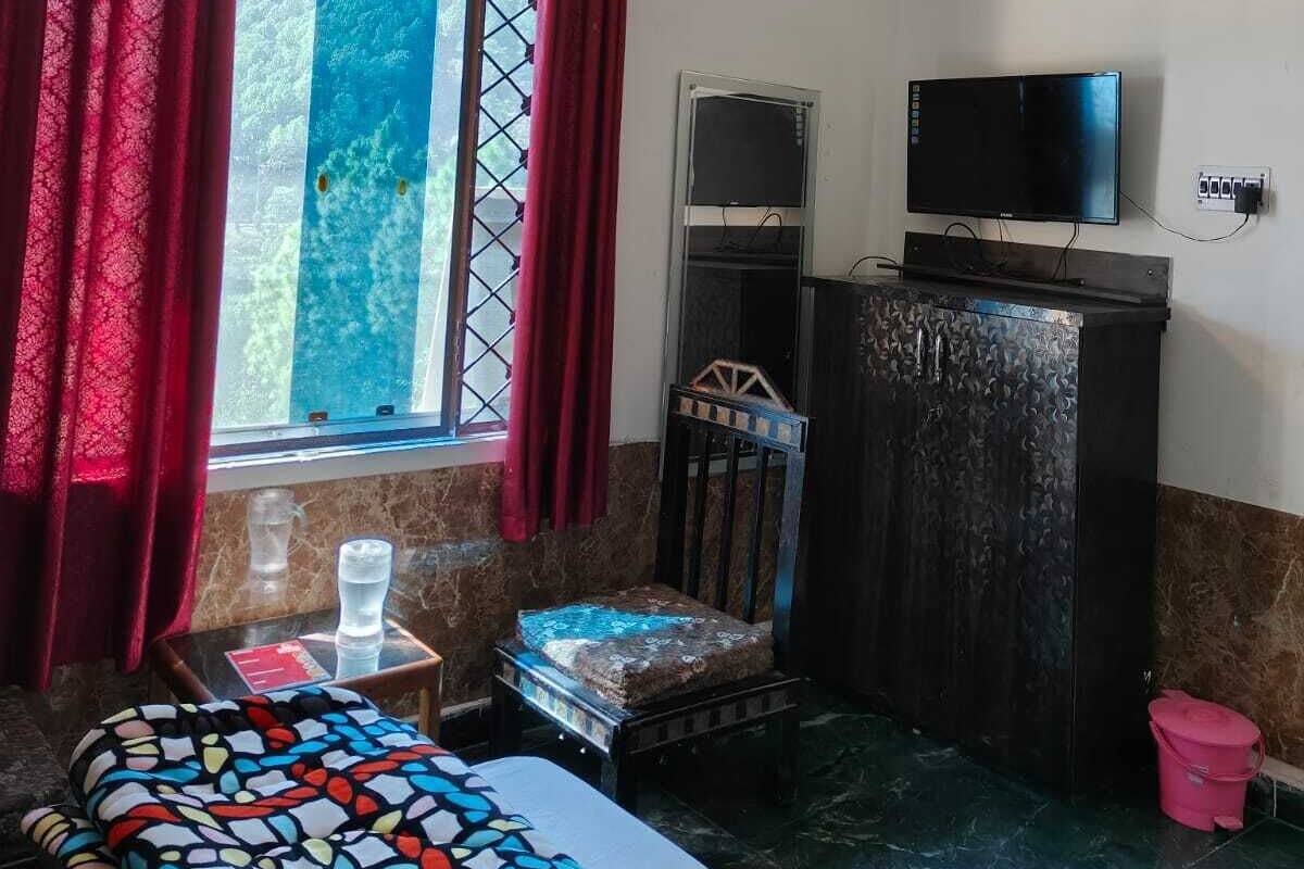 Un dormitori amb un llit, televisió, taula petita, finestra amb cortines i un armari.