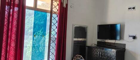 Un dormitorio con una cama, televisión, una mesita, ventana con cortinas y un armario.