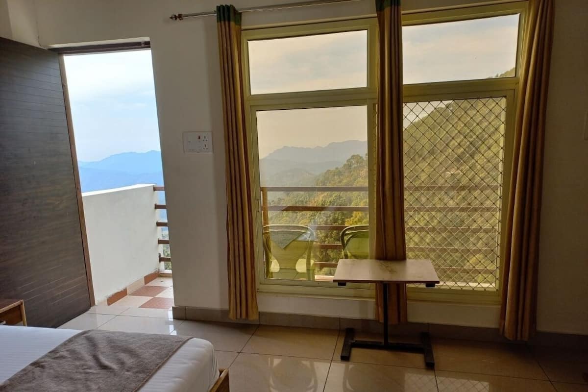Una habitació d'hotel amb llit, una taula petita i un balcó que mostra vistes a les muntanyes.