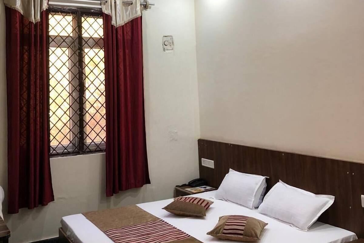 Habitació d'hotel amb un llit, una tauleta de nit, una finestra amb cortines, un ventilador de sostre i una làmpada.