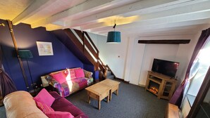 Ein gemütliches Wohnzimmer mit einem violetten Sofa, einem Holztisch und einem Fernseher auf einem Holzgestell.