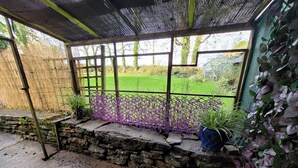Ein überdachter Patio-Bereich mit einer Steinmauer, einem Metallzaun und Blick auf ein grünes Feld.