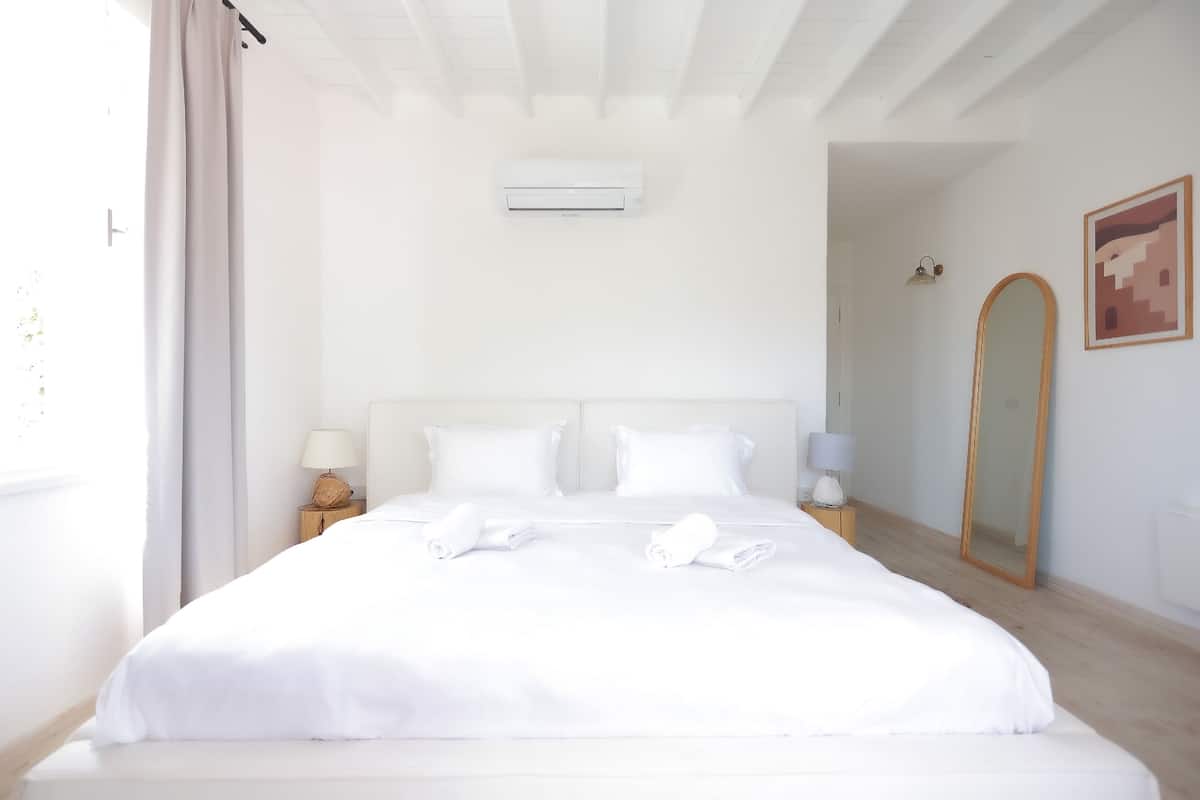 A hotel room with a large bed, two bedside lamps, a wall-mounted air conditioner, a mirror, and a framed picture on the wall.
