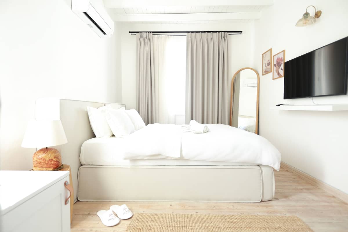 A modern bedroom with a bed, a flat-screen TV, a mirror, and a window with curtains.