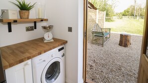 Una sala de bugaderia amb una rentadora, una balança, una cistella i una estant amb una planta i recipients.