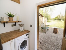 A laundry room with a washing machine, a scale, a basket, and a shelf with a plant and containers.