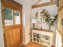 Una puerta de madera con un ventanal, una consola blanca con libros, un espejo y un florero con flores.