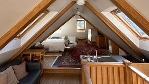 A cozy attic bedroom with a wooden ceiling, a bed, a sofa, a small table, and a window. - 1 Bed Suite - Sleeps 2, Patio, Parking & Wifi (St. Brelade)