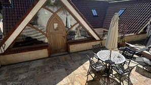 A patio with a round table and chairs, a wooden door, and a tiled roof. - 1 Bed Suite - Sleeps 2, Patio, Parking & Wifi (St. Brelade)