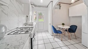 Une cuisine de taille réduite, équipée d’une cuisinière à gaz, de meubles blancs et d’un sol carrelé.
