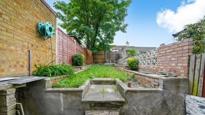 Une cour étroite, bordée d’un mur de briques, d’une clôture en bois et agrémentée d’un petit jardin.