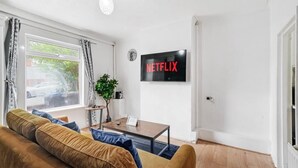 Un salon avec un canapé, une table basse, une plante et un téléviseur fixé au mur qui affiche le logo de Netflix.