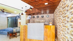 A reception area with a wooden reception desk, a blue sofa, a fan, and a wall with clocks. - Hotel Crystal Inn (Mumbai)