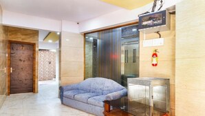 A modern lobby with a sofa, a glass table, a fire extinguisher, and a television mounted on the wall. - Hotel Crystal Inn (Mumbai)