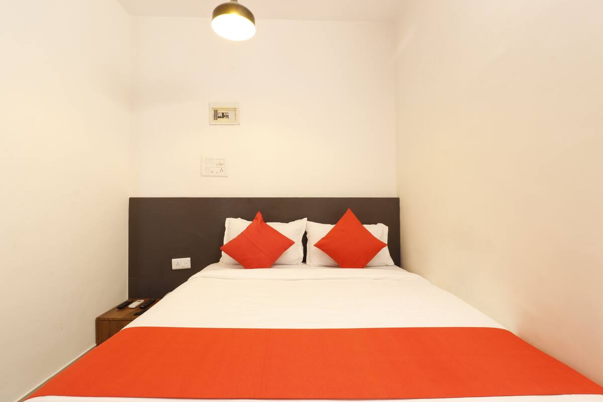 A neatly made bed with white and orange bedding, a dark headboard, and a small bedside table with a lamp.