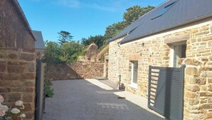 A stone building with a gravel driveway, a wooden gate, and a stone wall in the background. - House (Maupertus-sur-Mer)