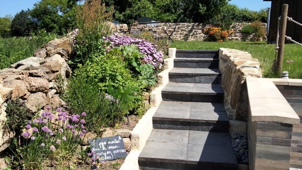 A stone staircase leading up to a building, surrounded by a garden with purple flowers and a sign in a foreign language. - House (Maupertus-sur-Mer)