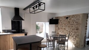 A modern kitchen with a large island, a stone wall, and a flat-screen TV mounted on the wall. - House (Maupertus-sur-Mer)