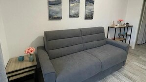 A modern living room with a grey sofa, a small wooden side table, and three abstract paintings on the wall. - Charming apartment 2 minutes from the beach (Vallauris)