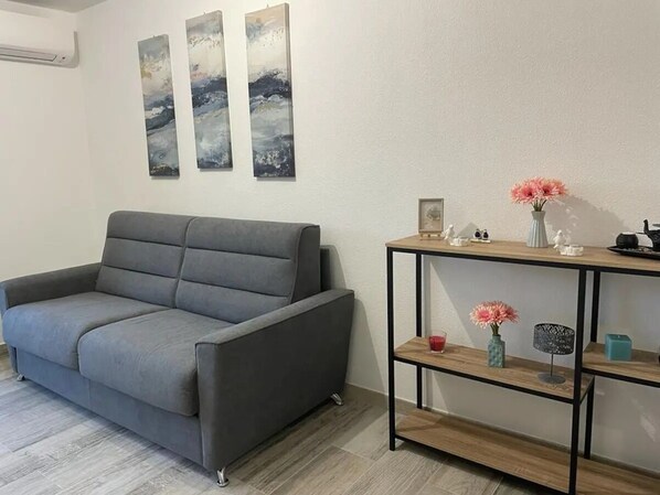 Ett vardagsrum med en grå soffa, ett träbord med dekorativa föremål och abstrakt konst på väggen.