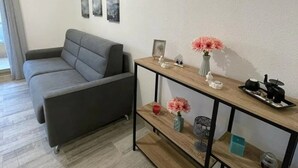 A modern living room with a grey sofa, a wooden coffee table, and a wall-mounted shelf with decorative items. - Charming apartment 2 minutes from the beach (Vallauris)