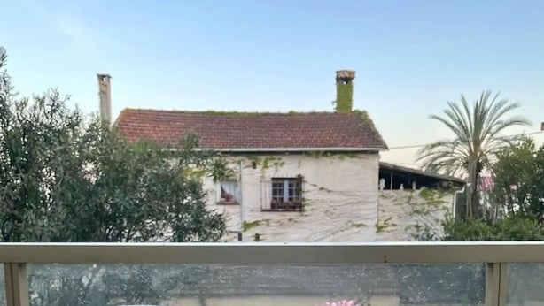 A balcony with a white chair and a table, a vase with pink flowers, and a view of a building with a red roof. - Charming apartment 2 minutes from the beach (Vallauris)