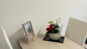 A small, square wooden table with a single chair. A framed picture and a potted plant with red flowers are on the table. - Charming apartment 2 minutes from the beach (Vallauris)