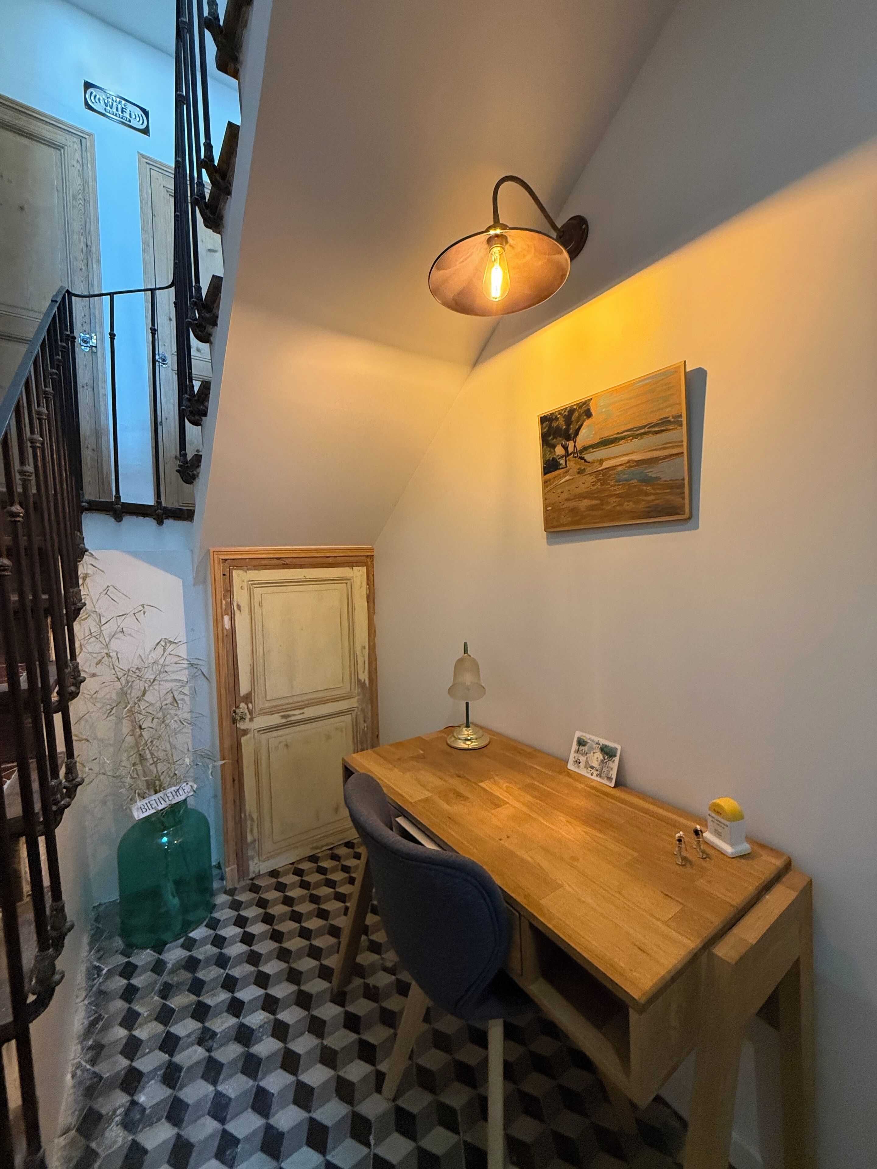 A dining area with a wooden table, a chair, a wall-mounted lamp, and a painting.