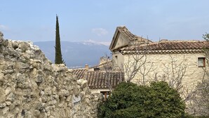 Un bâtiment en pierre avec un toit en tuiles, un grand arbre et une chaîne de montagnes en arrière-plan.
