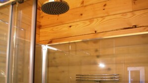 Una ducha con cerramiento de vidrio, techo de madera y un perchero metálico.