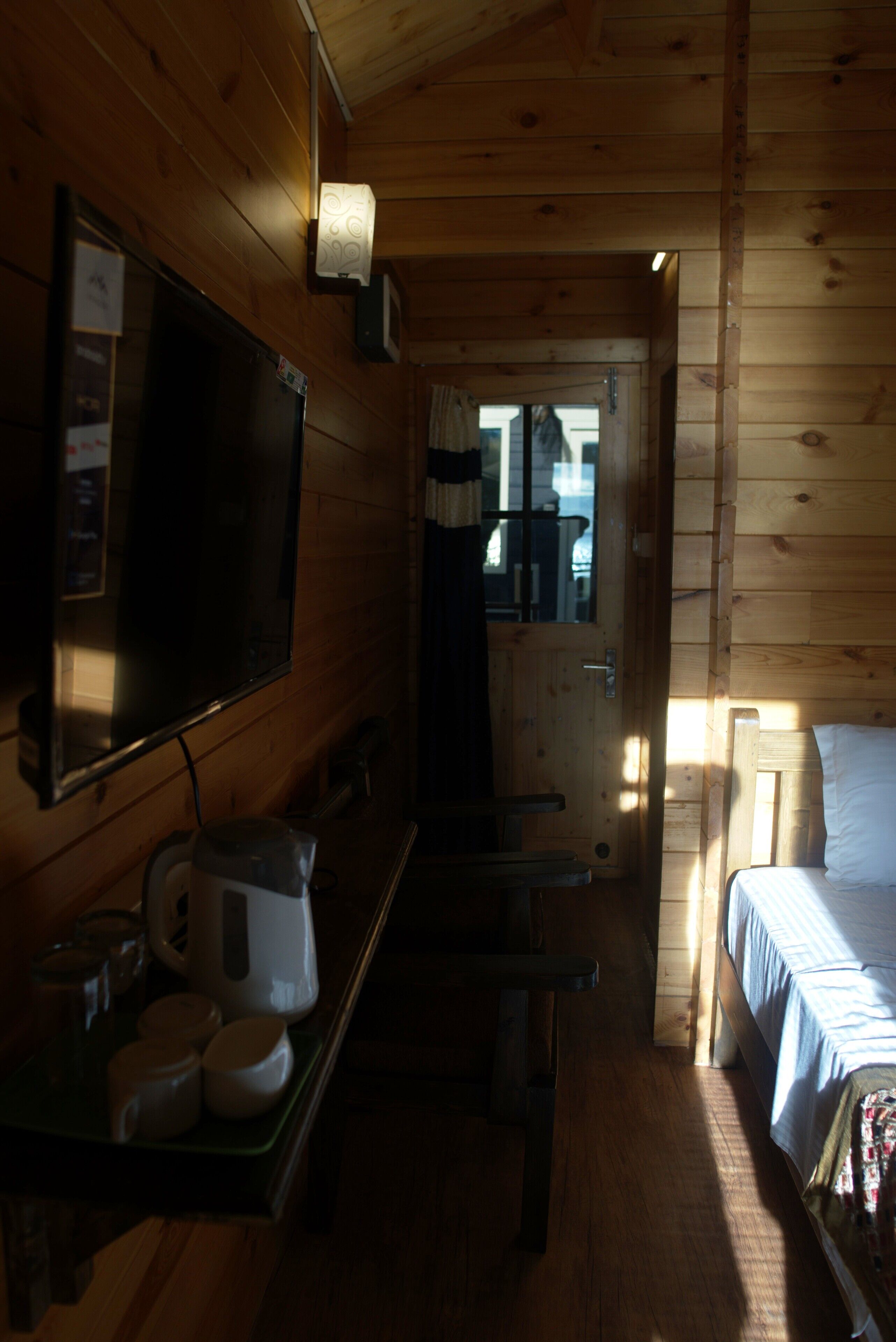A wooden cabin interior with a bed, a television, a coffee maker, and a door leading outside.