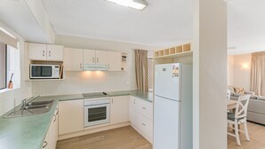 Cozinha compacta com micro-ondas, fogão e geladeira. Há uma área de refeições com mesa e cadeiras.