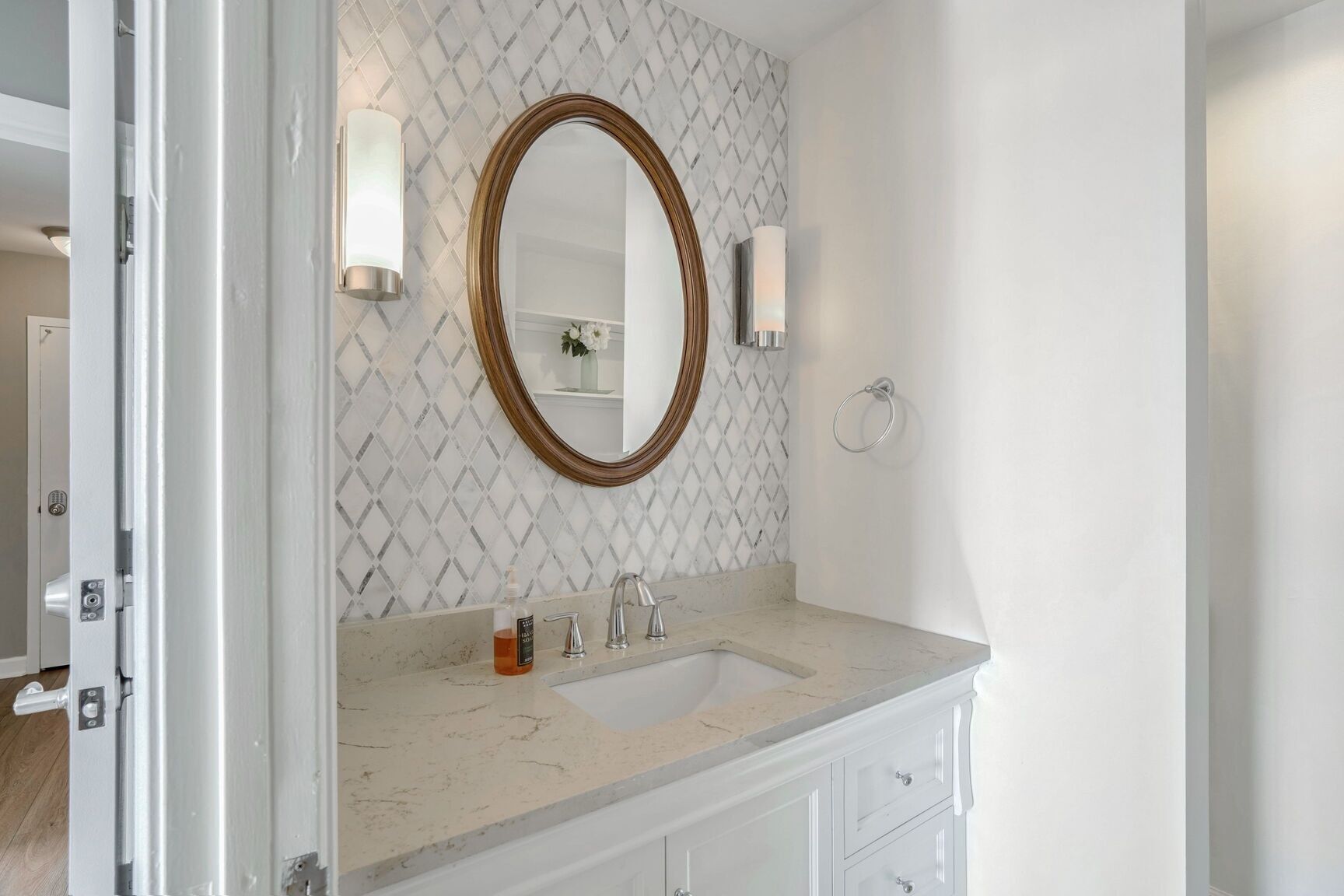Une salle de bain avec un lavabo en marbre, un grand miroir et un mur orné d’un motif.