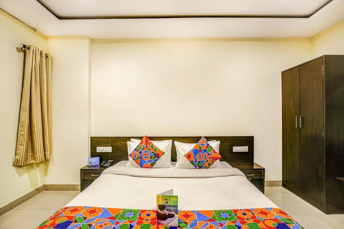 A hotel room with a bed, two pillows, a nightstand, a wardrobe, and a curtain.