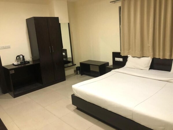 Habitación de hotel con una cama grande, un armario, un escritorio con hervidor y una mesita pequeña.