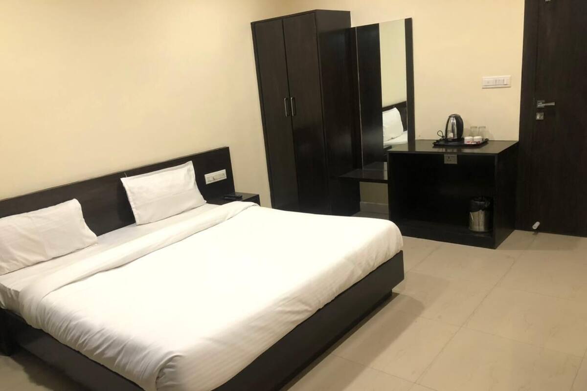 A modern bedroom with a bed, a wardrobe, a desk with a mirror, and a small table with a kettle.
