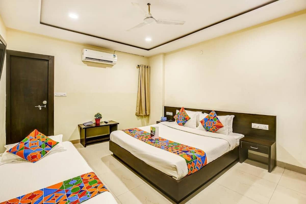 A hotel room with a large bed, a bedside table, a nightstand, an air conditioning unit, a ceiling fan, and a door.