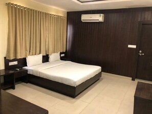A modern hotel room with a large bed, dark wood paneling, an air conditioning unit, and a door with a handle. - Hotel Imperial Udaipur (Udaipur)