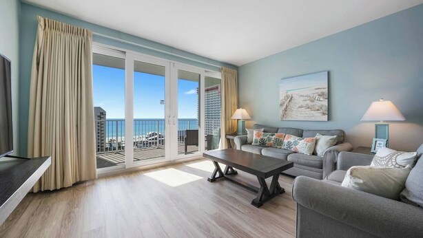 A modern living room with a large sliding glass door leading to a balcony with a view of the ocean. There is a sofa set, a coffee table, and two lamps. - Laketown Wharf 822- 2BR, Oceanview (Panama City Beach)