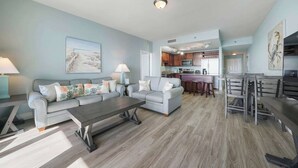 A spacious living room with a grey sofa, a coffee table, and a kitchen in the background. - Laketown Wharf 822- 2BR, Oceanview (Panama City Beach)