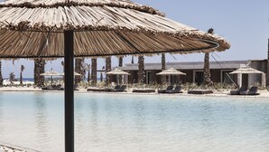 A beachside lounge area with a thatched umbrella, lounge chairs, and a pool. - Casa Cook North Coast -  Adults only (El Alamein)