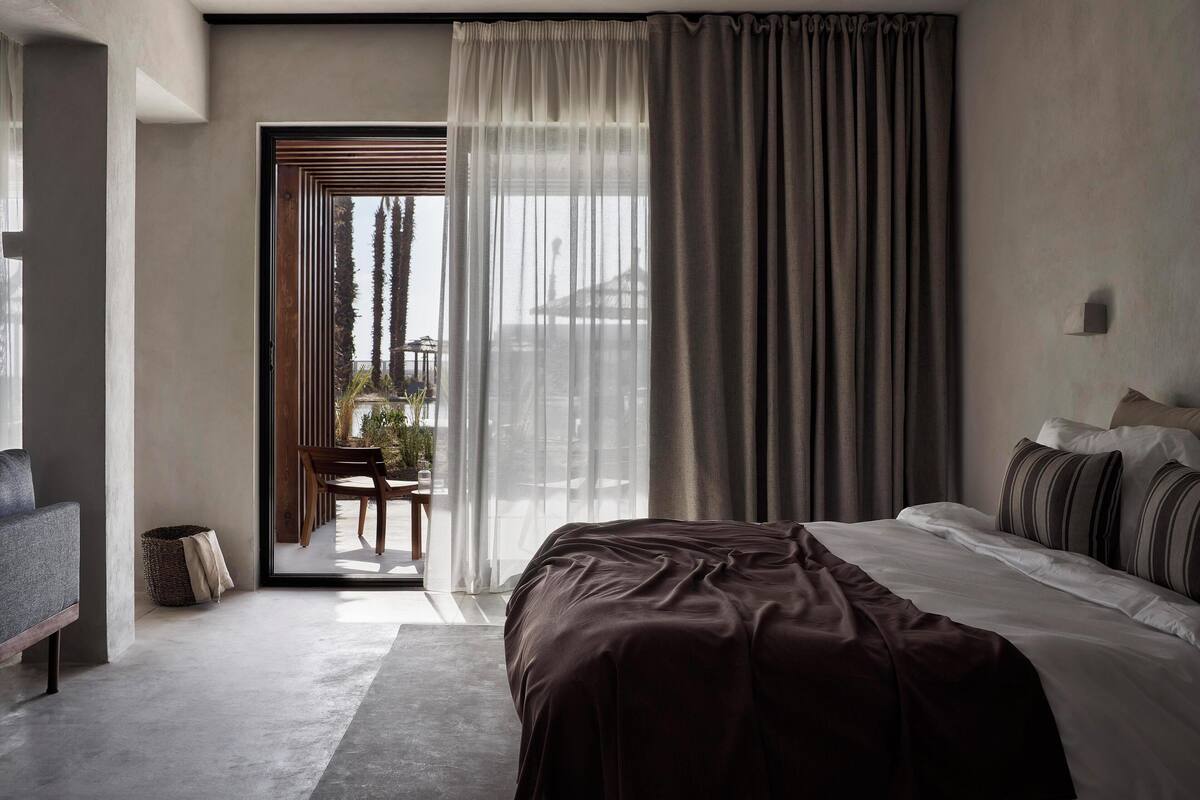 A modern bedroom with a large bed, a sofa, and a view of the outdoors through a sliding door.