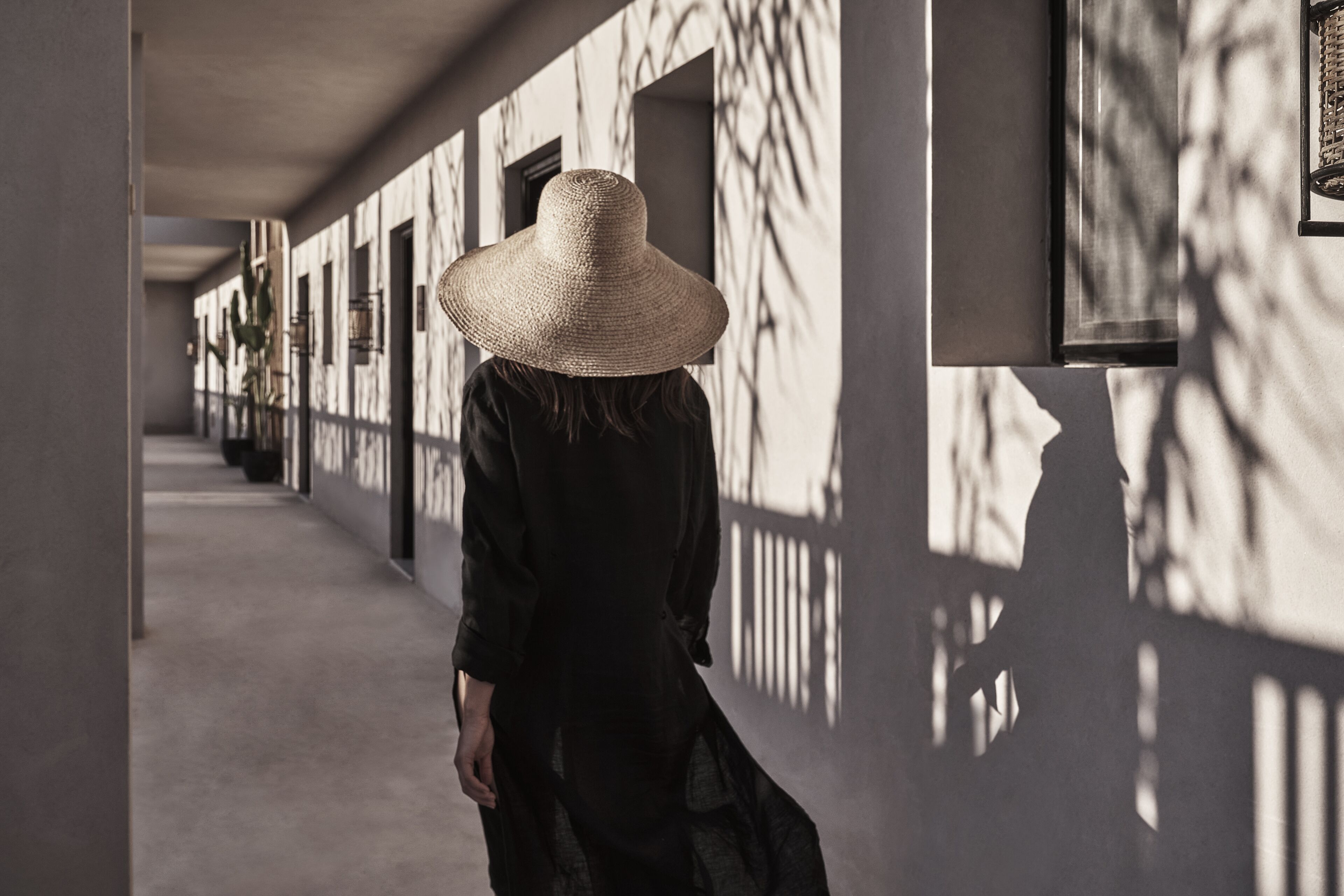 Un pasillo con una persona que se aleja, usando un sombrero de ala ancha.