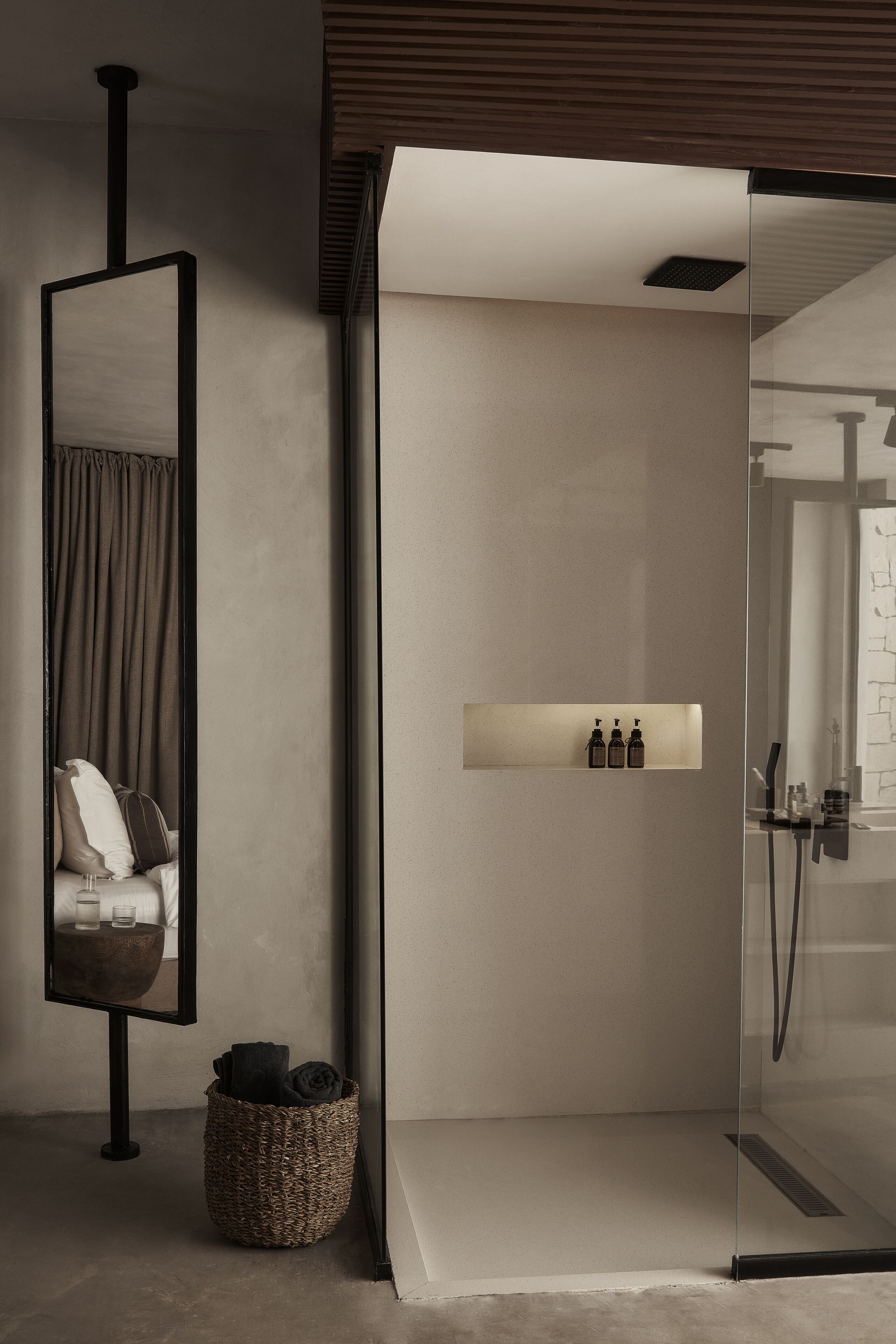 A modern bathroom with a glass shower enclosure, a mirror, a shelf with toiletries, and a woven basket.