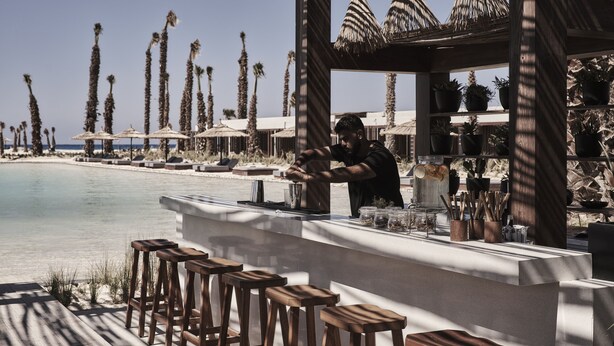 A beachside bar with wooden stools and a bartender preparing drinks. - Casa Cook North Coast -  Adults only (El Alamein)